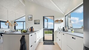 Une cuisine moderne dotée d’un grand îlot central, de luminaires suspendus et offrant une vue sur l’extérieur.