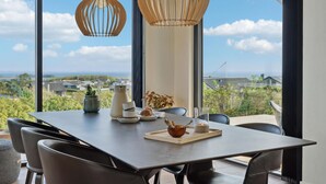 Un coin repas avec une table dressée pour quatre personnes, de grandes fenêtres offrant une vue sur le paysage et deux lampes suspendues.