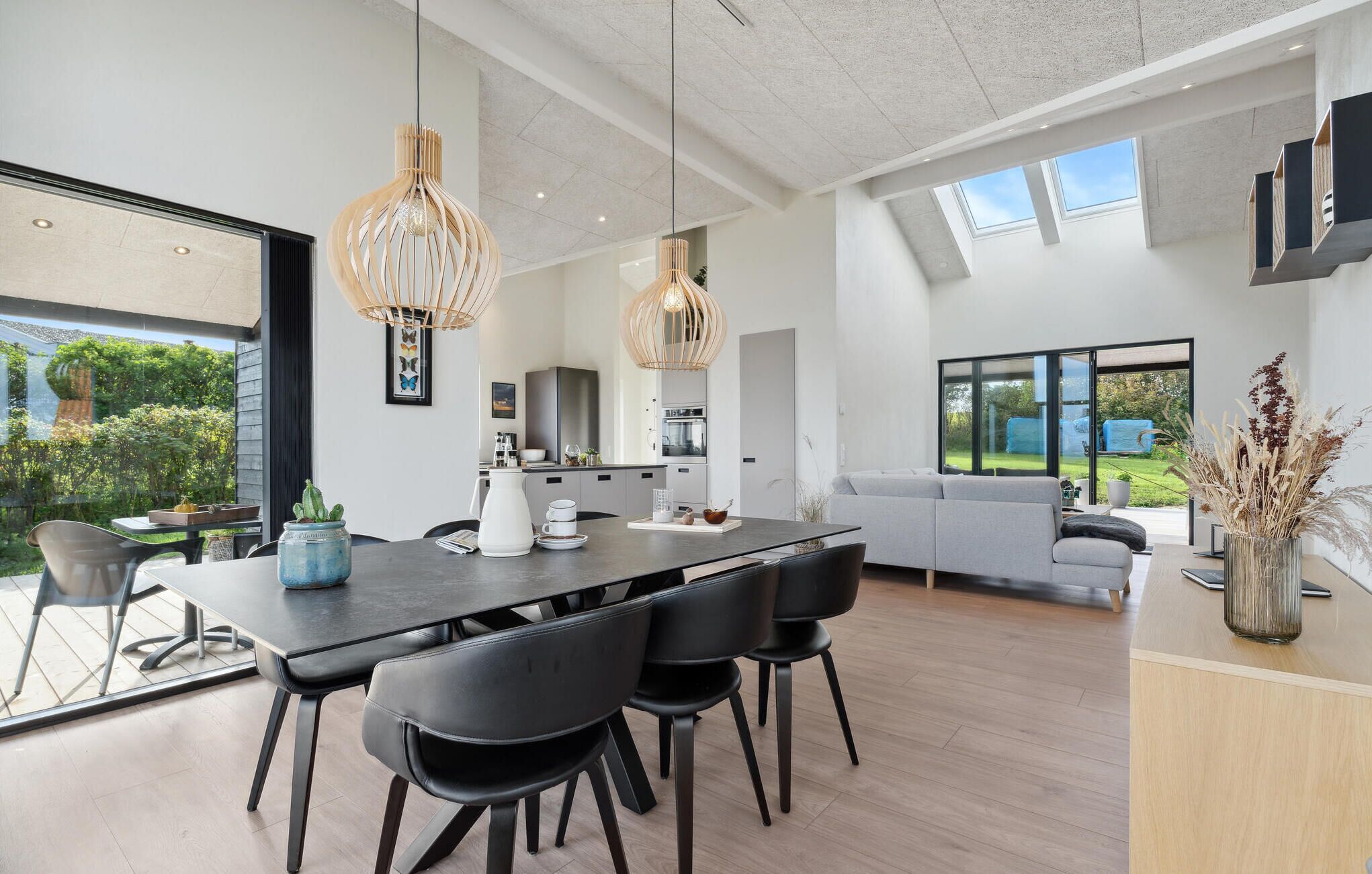Une cuisine moderne avec un coin repas, comprenant une grande table, des chaises noires et des luminaires suspendus.