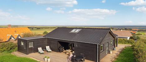 Ein modernes Haus mit einer Terrasse, Sitzgelegenheiten im Freien und Blick aufs Meer.