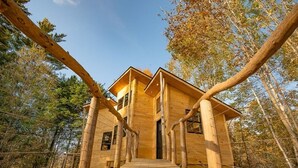 A wooden cabin with a central staircase leading to a door, surrounded by trees. - Luxury Treehouse central Stowe/Waterbury. Borders State park. Walk to the Lake! (Waterbury Center)