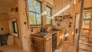A wooden cabin interior with a kitchen, dining area, and a window overlooking the outdoors. - Luxury Treehouse central Stowe/Waterbury. Borders State park. Walk to the Lake! (Waterbury Center)