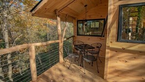 A wooden cabin with a balcony, metal chairs, and a table. - Luxury Treehouse central Stowe/Waterbury. Borders State park. Walk to the Lake! (Waterbury Center)