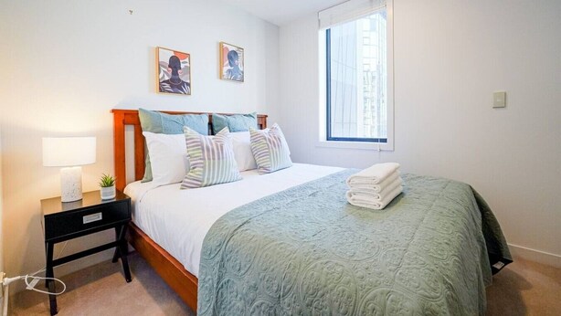 A bedroom with a bed, a nightstand, a lamp, a window, and two wall art pieces.