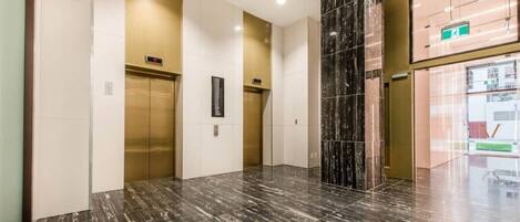 A modern elevator area with marble flooring and a glass wall.