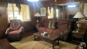 A cozy living room with a brown leather couch, a matching armchair, and a wooden coffee table. There are two lamps on side tables, a rug on the floor, and a large mirror on the wall. - Welcome to the Gathering Place! Where Families and friends can gather together.  (McKeesport)