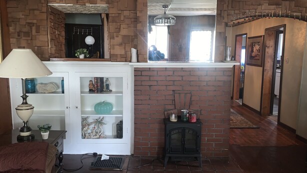 A living room with a fireplace, a white cabinet with shelves, a lamp, and a small black stove. - Welcome to the Gathering Place! Where Families and friends can gather together.  (McKeesport)