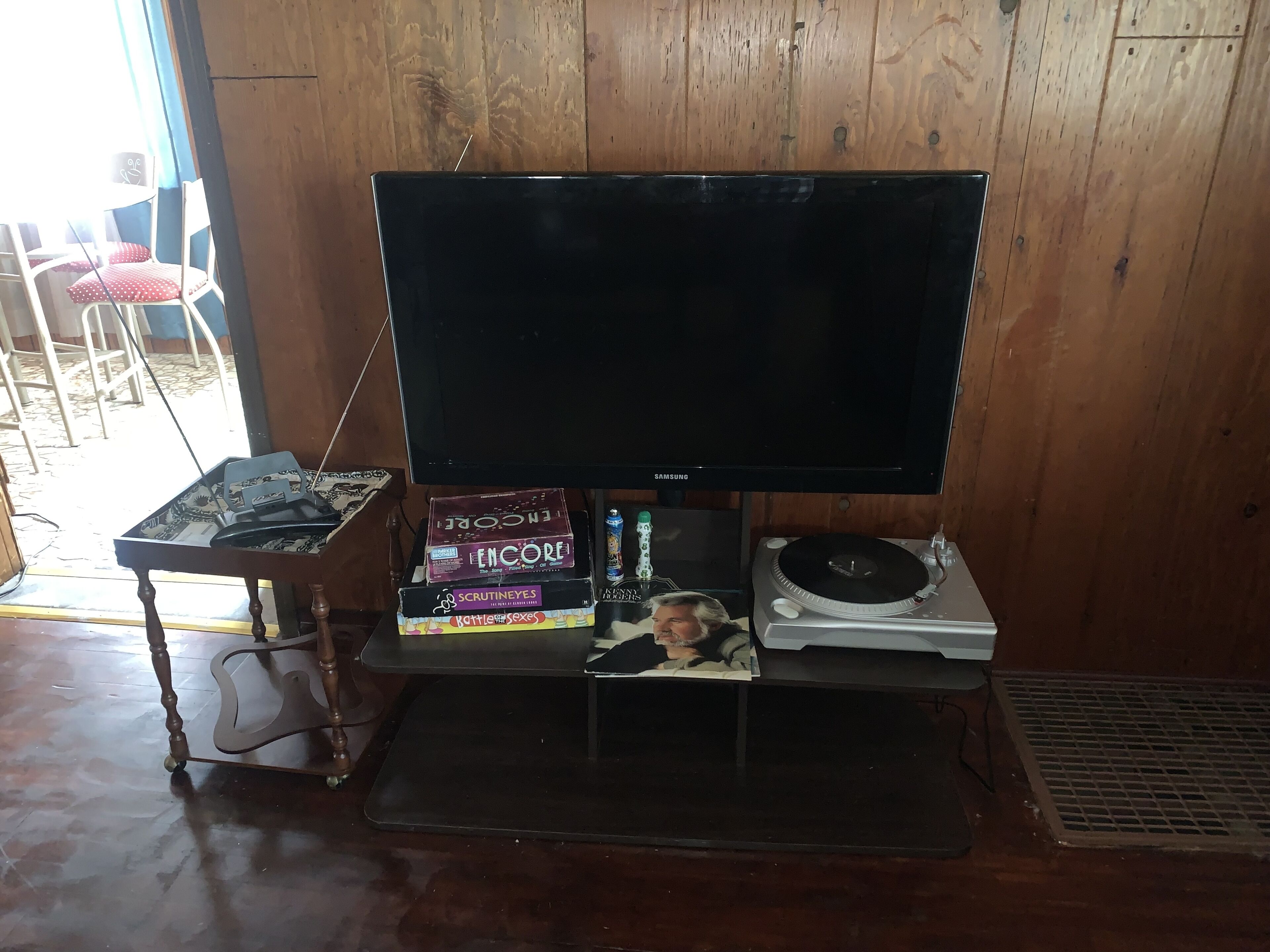 A room with a wooden floor, a television on a stand, a small table with a keyboard and mouse, and a few books.