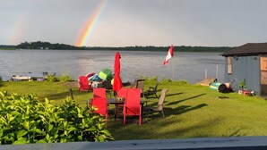 A lakeside patio with outdoor furniture, a flag, and a rainbow. - Sunrise net on Pigeon Lake 4 season cottage (Kawartha Lakes)