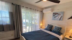 A bedroom with a bed, curtains, a ceiling fan, a nightstand, and a wall-mounted lamp. - Sunrise net on Pigeon Lake 4 season cottage (Kawartha Lakes)