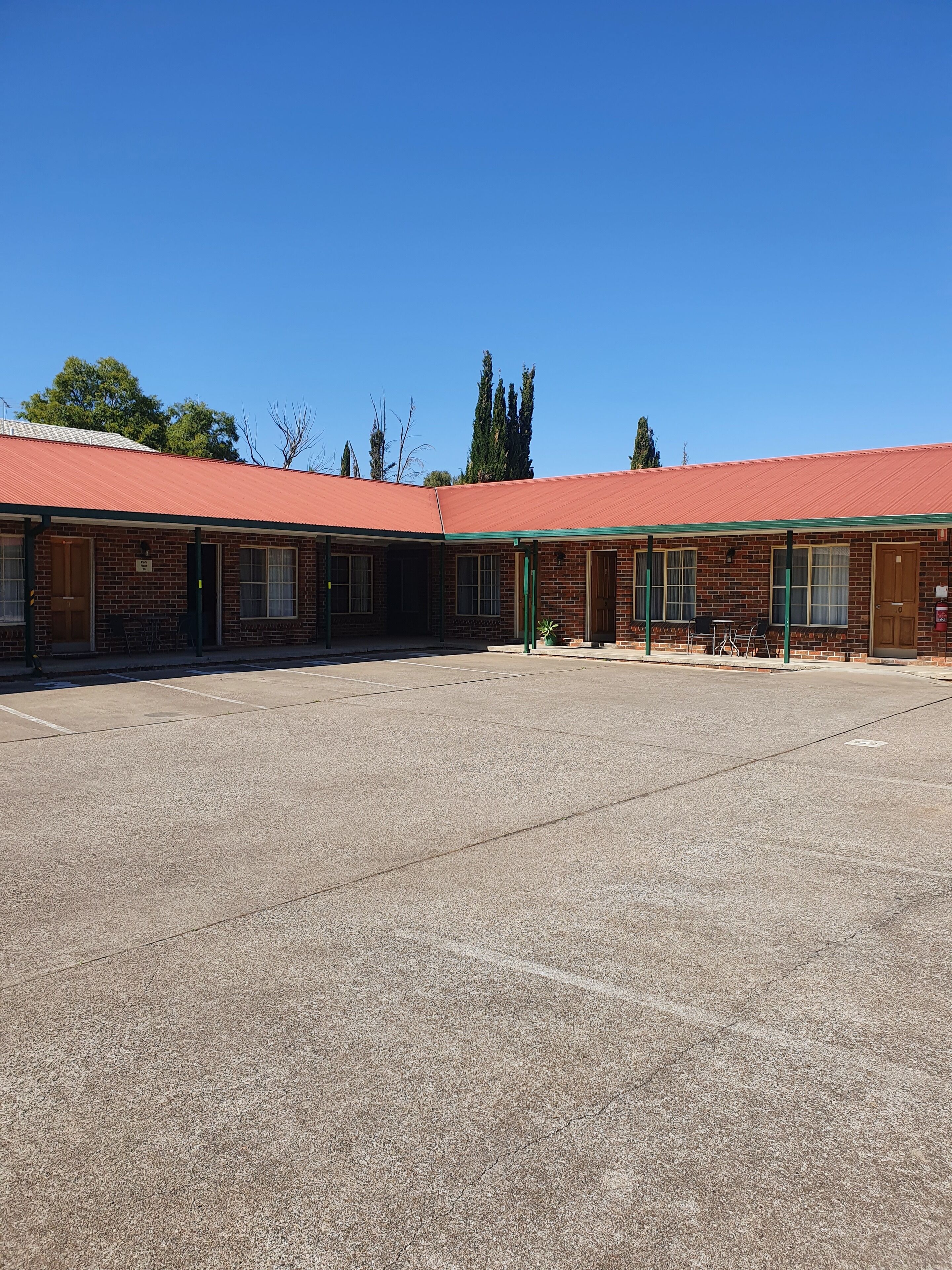A row of single-story brick buildings with a red roof, a parking lot, and a clear blue sky.