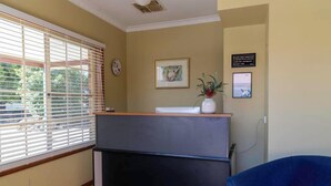 A reception area with a desk, a blue chair, a clock, and a framed picture on the wall. - ALYN MOTEL (Gunnedah)