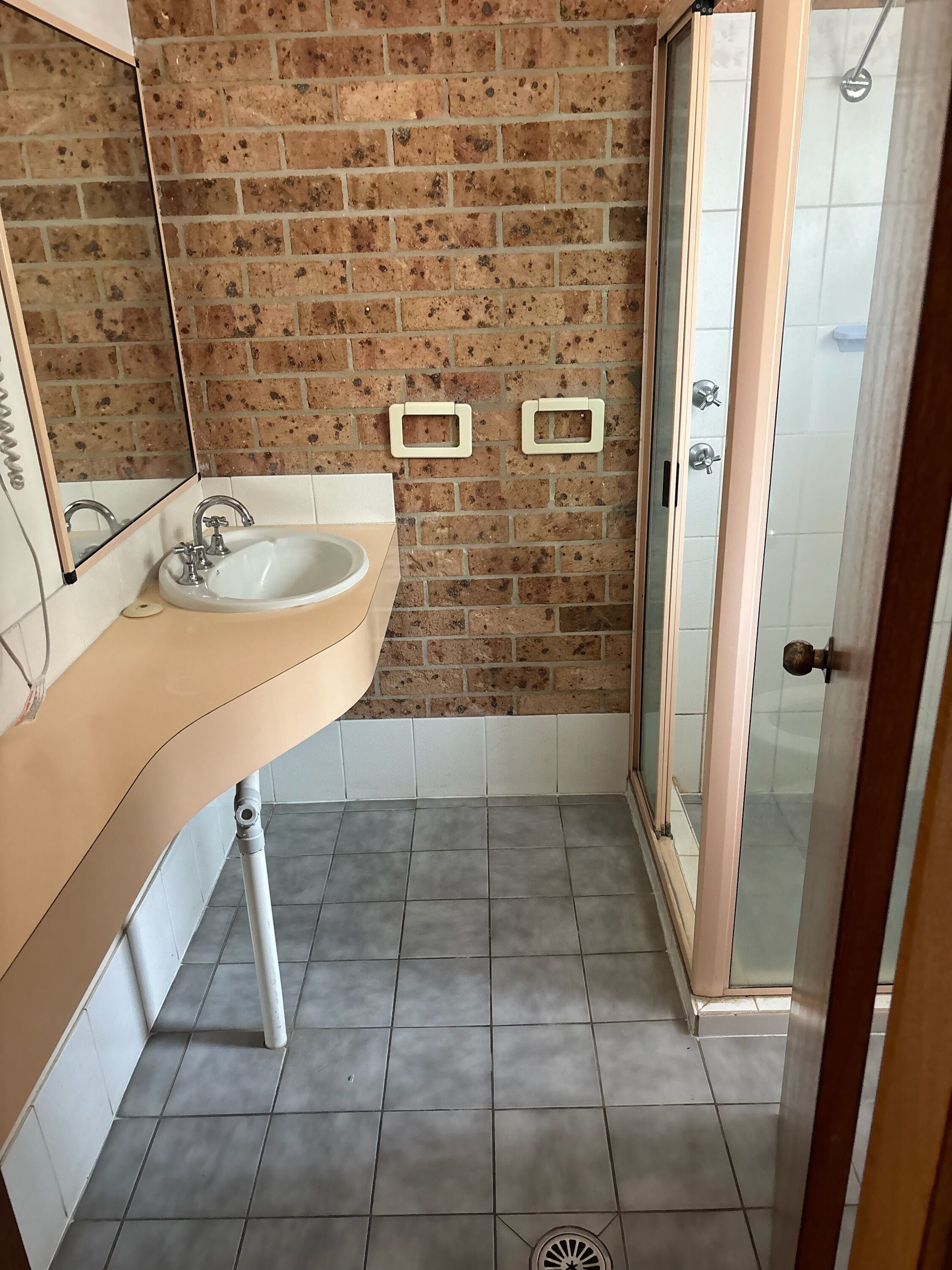 A bathroom with a white sink, a mirror, a shower with a glass door, and a brick wall.