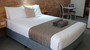 A neatly made bed with a headboard, a small table with chairs, and a brick wall. - ALYN MOTEL (Gunnedah)