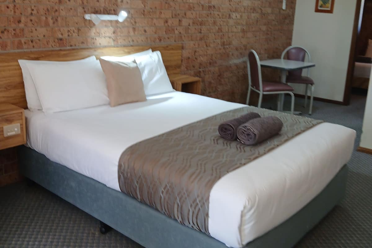 A neatly made bed with a headboard, a small table with chairs, and a brick wall.