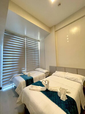A hotel room with two beds, a large window with blinds, and a ceiling light. - One bedroom Unit at mactan newtown (Lapu-Lapu)