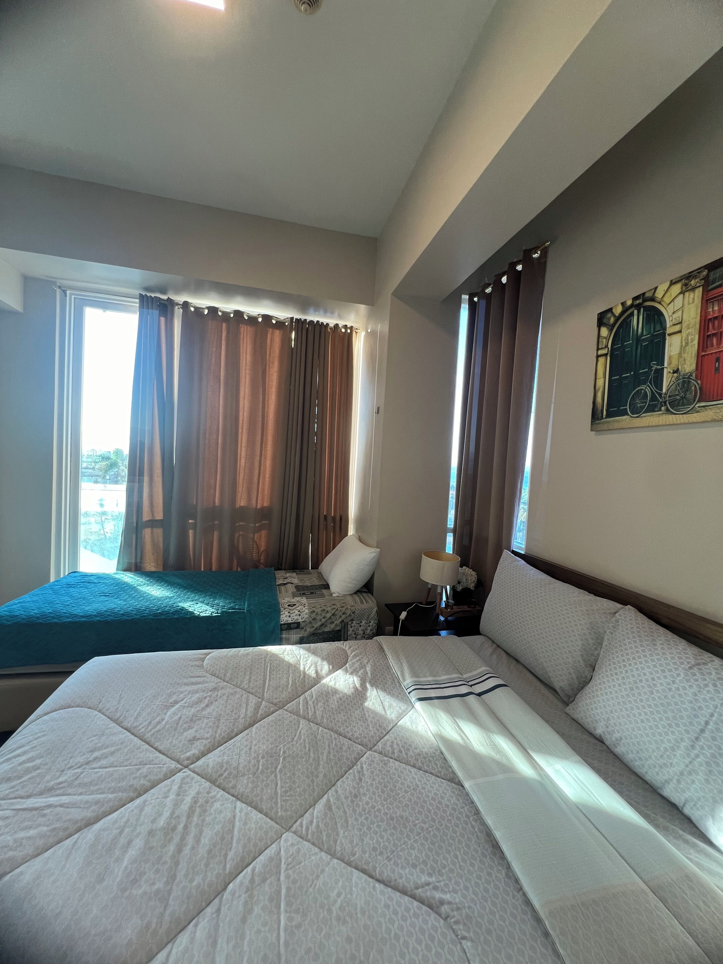 Habitación de hotel con una cama grande, una cama más pequeña, un escritorio con lámpara y un cuadro en la pared.