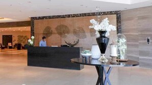 A reception area with a modern design, featuring a reception desk, a decorative wall with leaf patterns, and a table with a vase of flowers. - One bedroom Unit at mactan newtown (Lapu-Lapu)