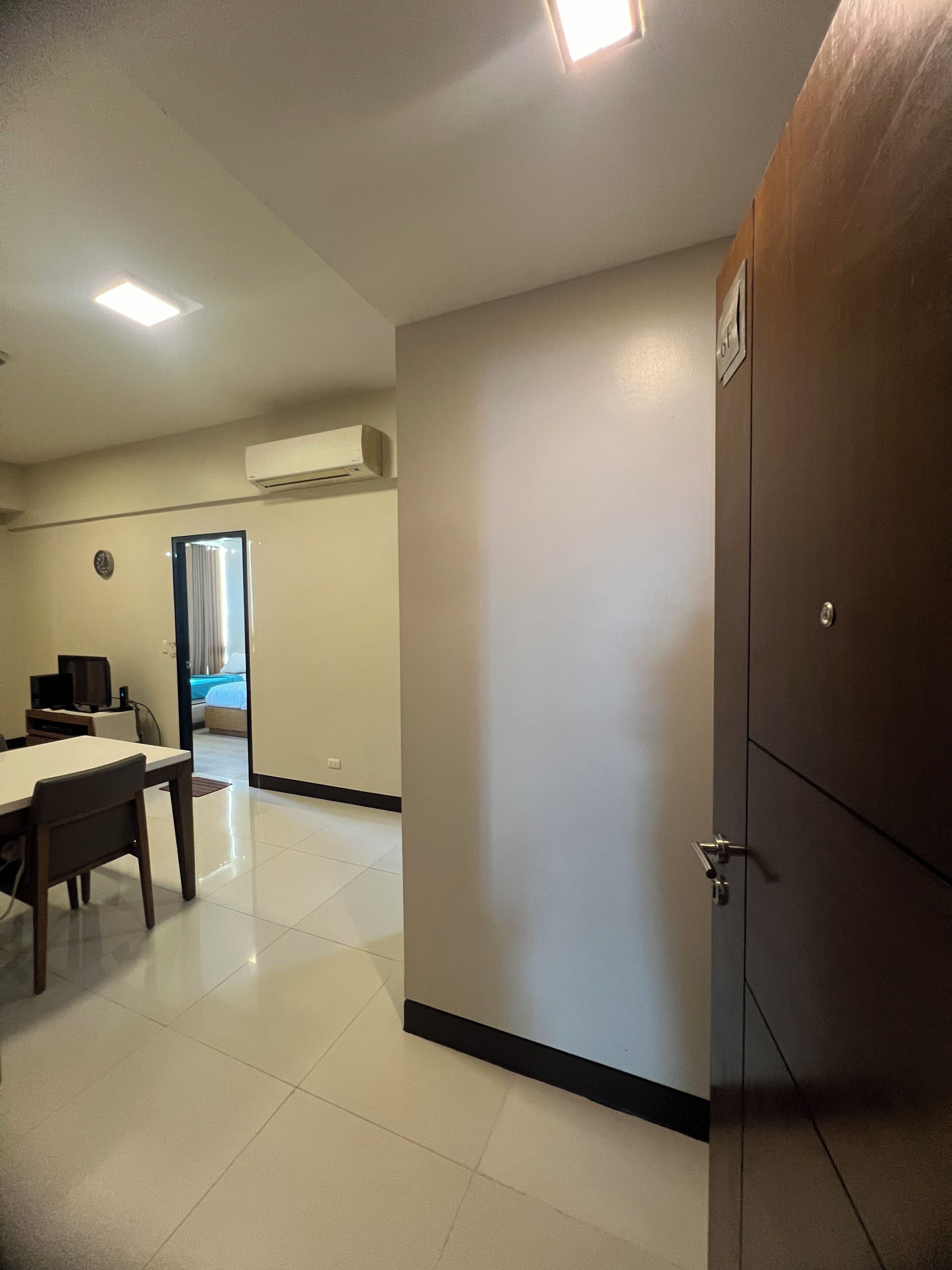 A hotel room with a bed, a desk, a chair, a TV, and an air conditioning unit.