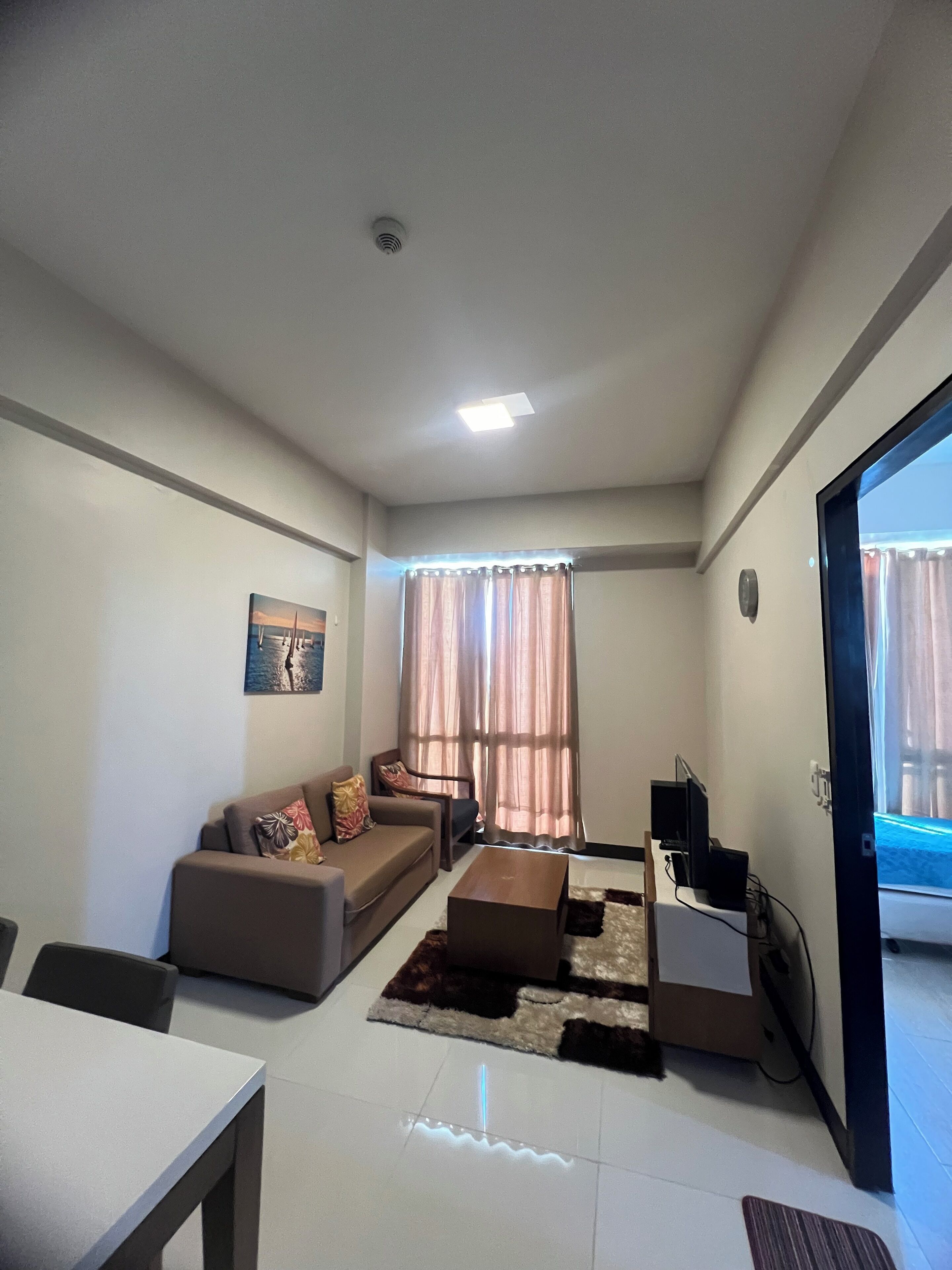 Una sala de estar con sofá, mesa de centro, mueble para televisor y ventana con cortinas.