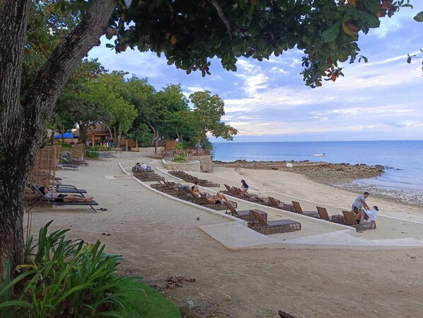 A beach with sun loungers and a thatched-roof building in the background. - One bedroom Unit at mactan newtown (Lapu-Lapu)