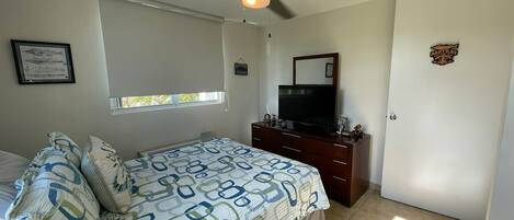 A bedroom with a bed, a dresser, a television, a ceiling fan, a window, and a door.