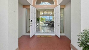 Entrada de hotel con un felpudo que dice 'WELCOME', puerta de cristal y vista del interior, incluyendo una zona de estar y una planta.