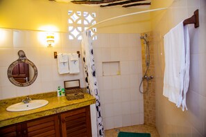 A bathroom with a sink, mirror, towel rack, shower, and a decorative wall panel. - Cottage Sleeps 2 - Pool, Parking, Beach Access (Diani Beach)