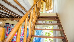 A wooden staircase with a thatched roof and patterned fabric hanging on the walls. - Cottage Sleeps 2 - Pool, Parking, Beach Access (Diani Beach)