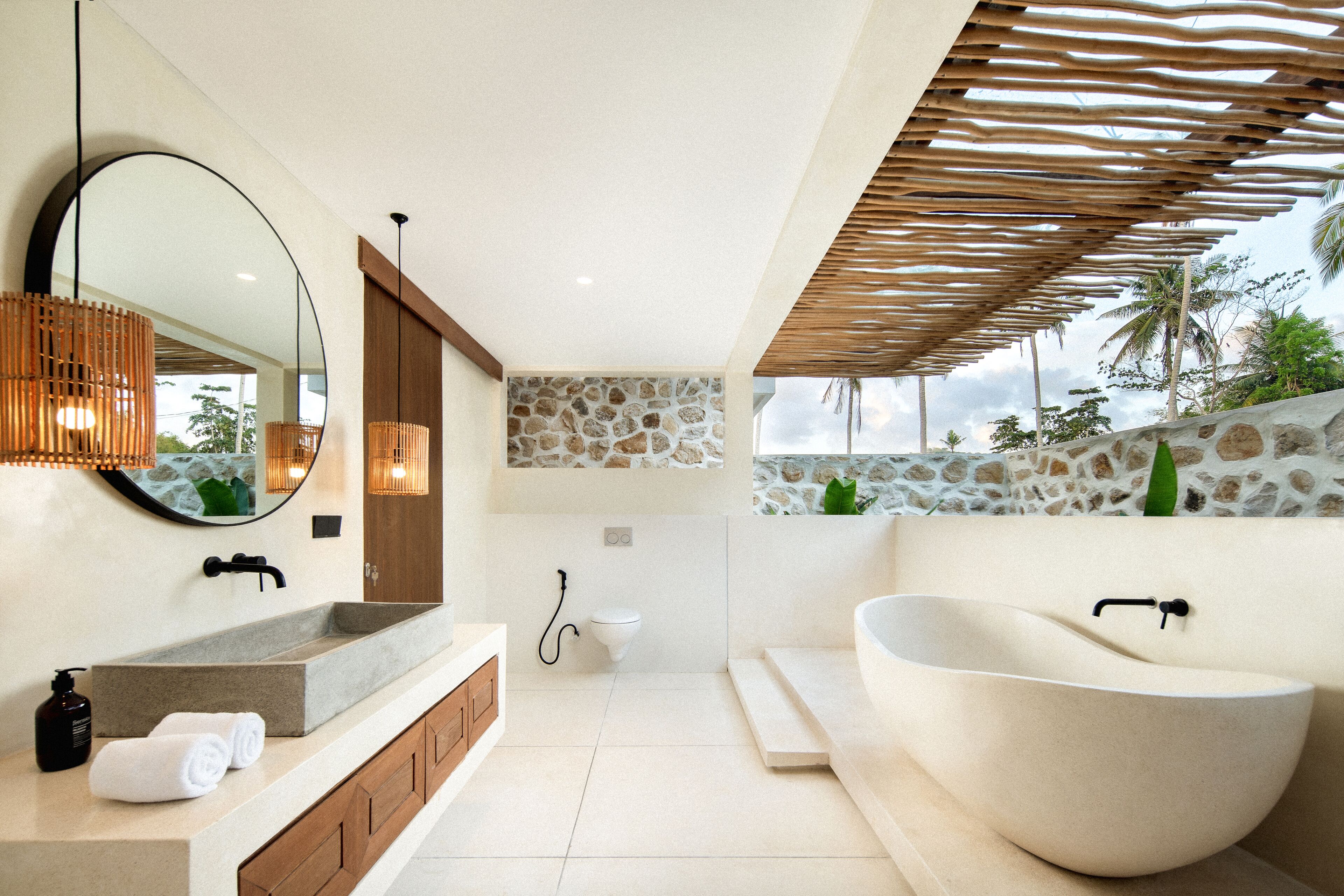 A modern bathroom with a large freestanding bathtub, a stone accent wall, and a wooden slatted ceiling.