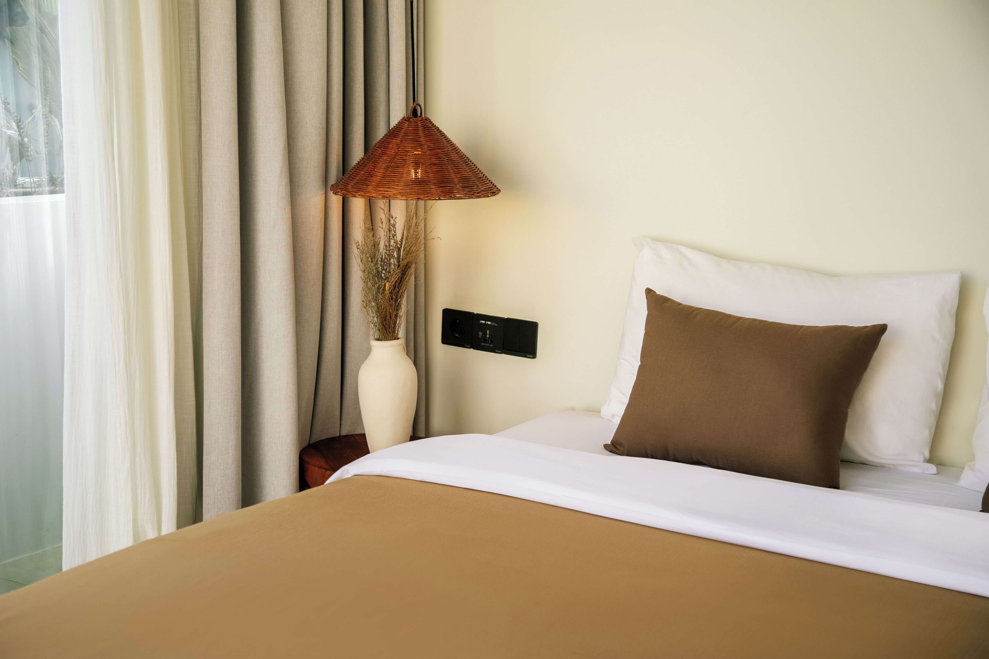 A hotel room with a bed, a lamp, a vase, and curtains.