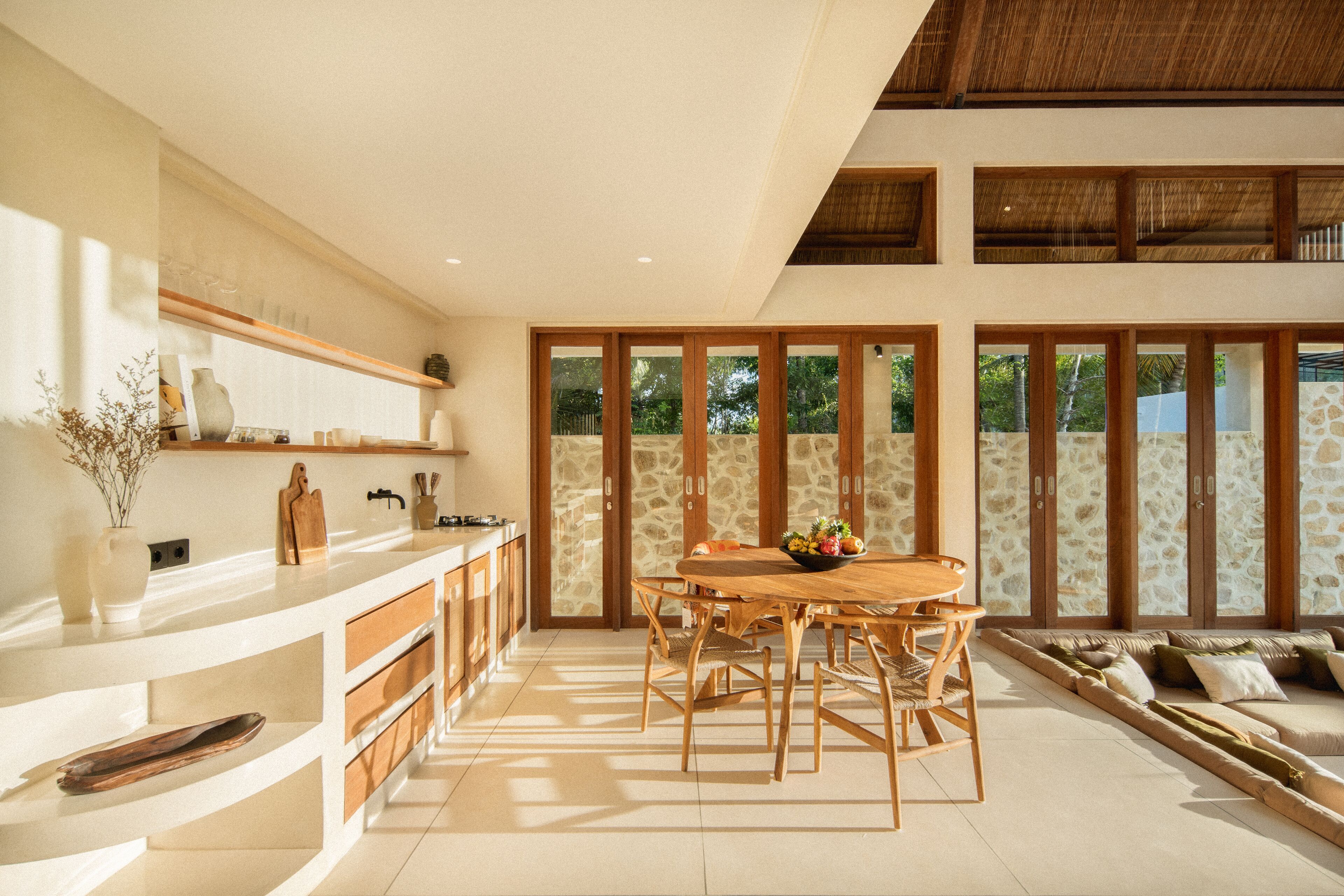 A spacious kitchen with a wooden dining table, built-in shelves, and a stone wall backdrop.