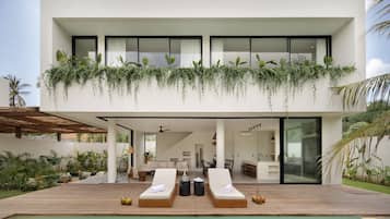 Un bâtiment moderne à deux étages doté d’une piscine, de chaises longues et d’un patio couvert.
