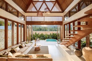 Amplia sala de estar con escalera de madera, piscina y vista a zonas verdes.