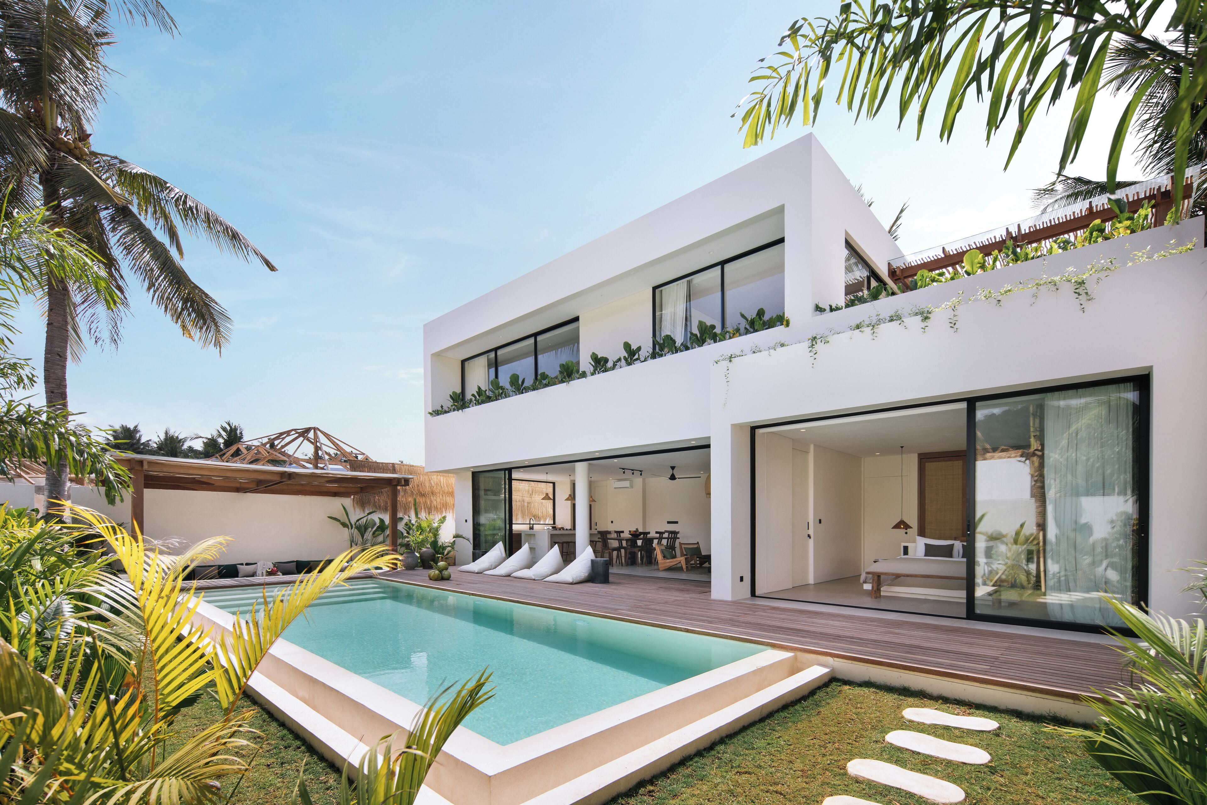 A modern two-story house with a swimming pool, outdoor seating, and lush greenery.