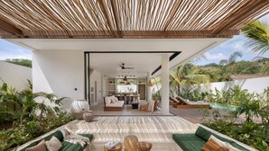 Un espace de vie extérieur moderne, comprenant un canapé, une table basse en bois et un coin repas visible à travers une porte ouverte.