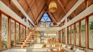 Un intérieur spacieux avec un plafond haut, des poutres en bois, un escalier et un coin repas.