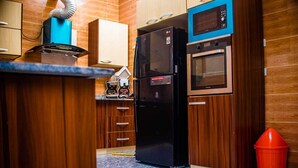 Une cuisine avec des meubles de rangement en bois, un réfrigérateur noir, un four à micro-ondes et une poubelle rouge.