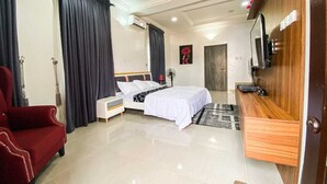 Une chambre d’hôtel avec un lit, un fauteuil rouge, une table d’appoint en bois, une télévision et une porte.