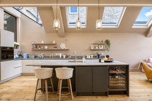 A modern kitchen with a central island, bar stools, a wine rack, and skylights.