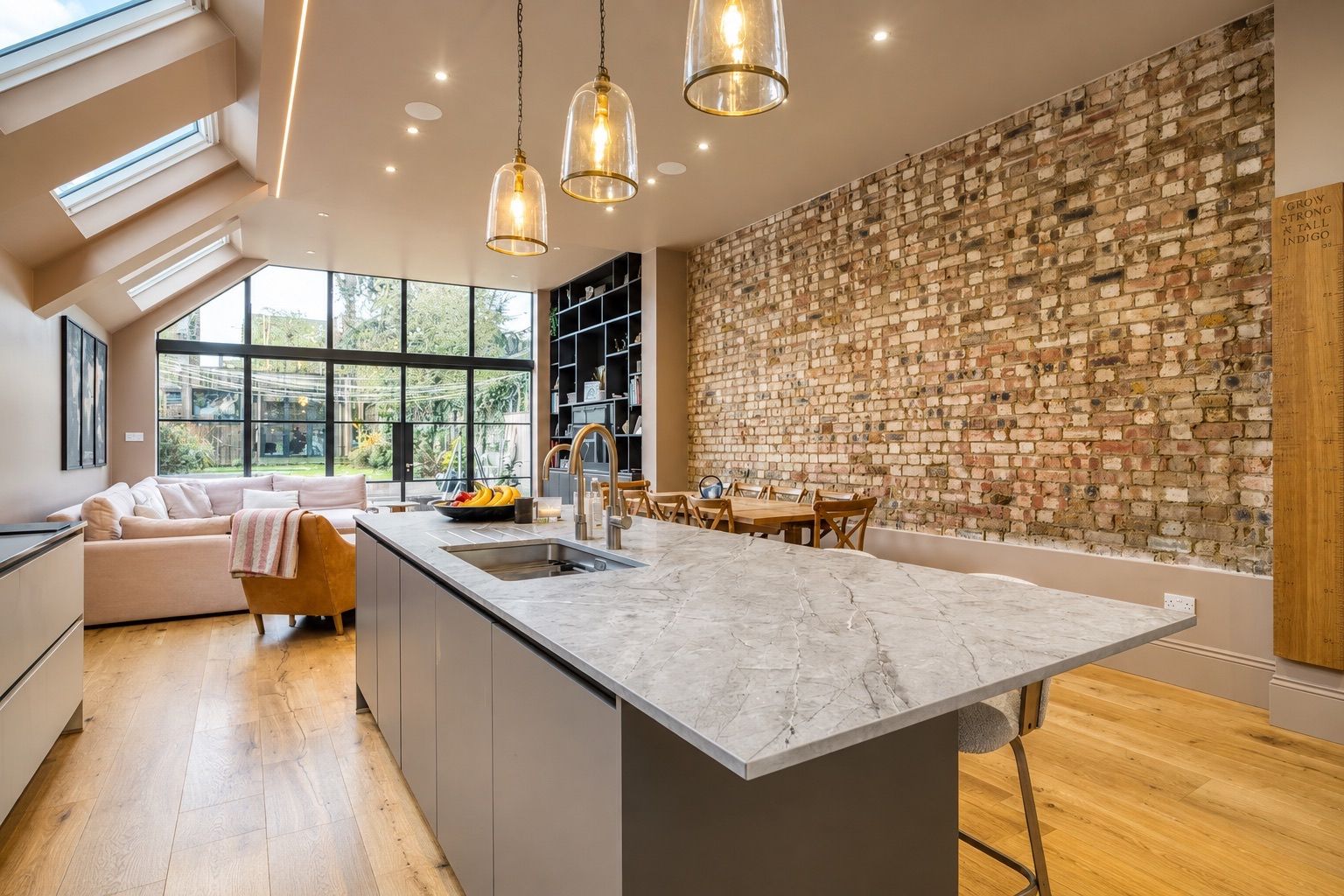 Una cocina moderna con una isla de mármol, luces colgantes y una pared de ladrillo.