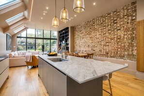 A modern kitchen with a marble island, pendant lights, and a brick wall.