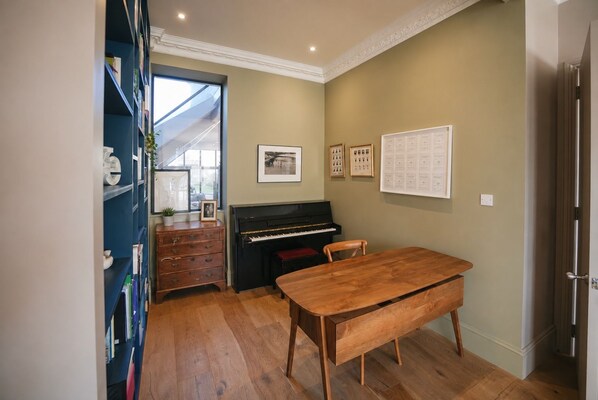 A room with a piano, a wooden table, and a bookshelf.