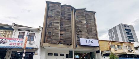 Un hotel con fachada moderna, un cartel que dice 'INK' y varios coches aparcados adelante.