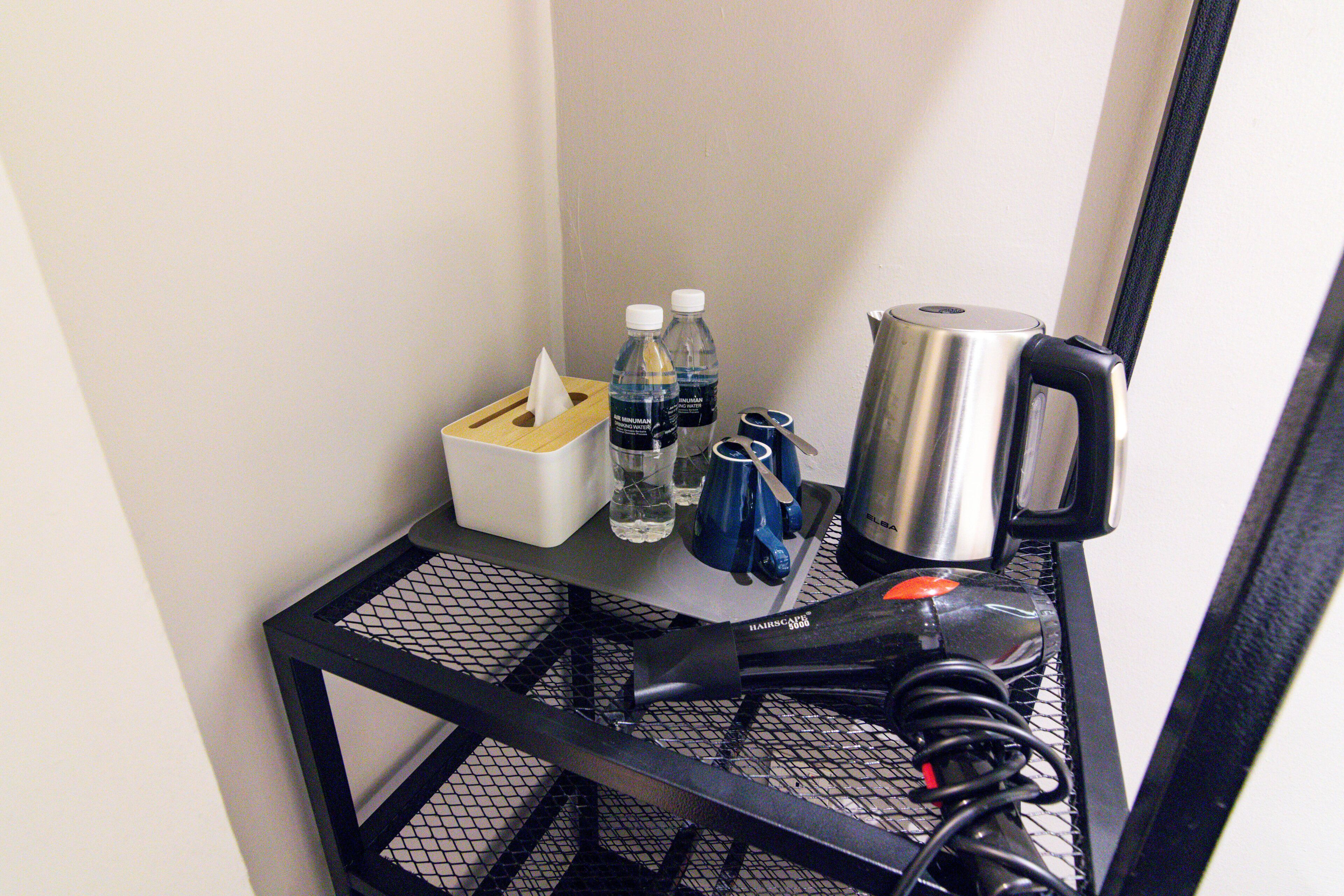 A small table with a hairdryer, two bottles of water, a coffee mug, and a tissue box.