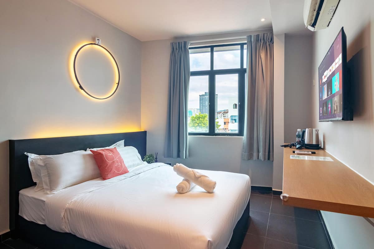 A hotel room with a bed, a TV, a window with curtains, and a wall-mounted air conditioner.