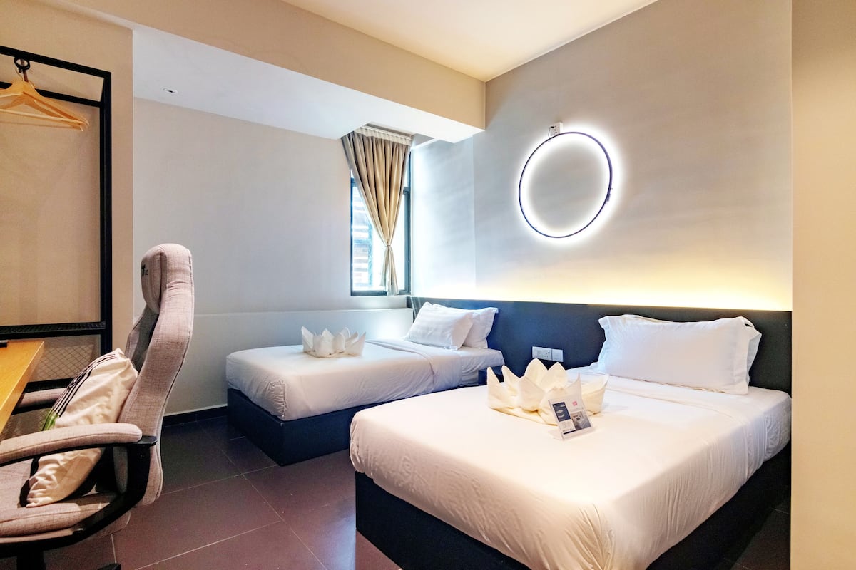 A hotel room with two beds, a chair, a desk, and a window with curtains.