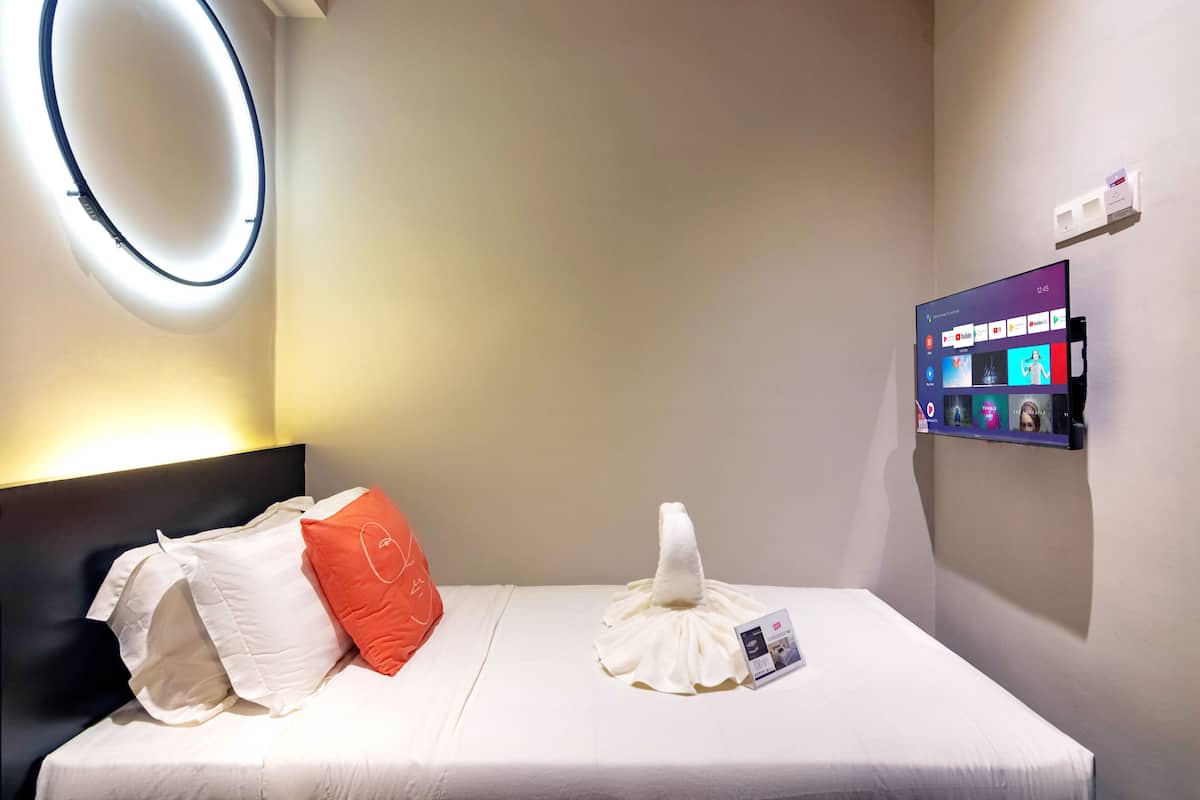 A hotel room with a bed, pillows, a towel, a wall-mounted TV, and a circular light fixture.