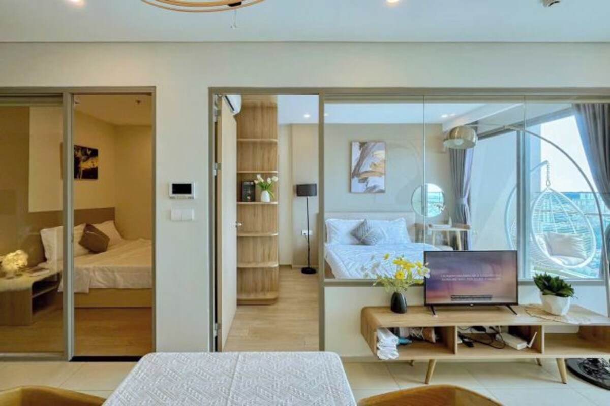 A modern hotel room with a bed, a desk with a laptop, a TV, and a large window with a view of the city.