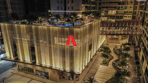 Et moderne hotel med et markant rødt 'A'-logo, der har en taghave og en veloplyst atriumgård med palmer.